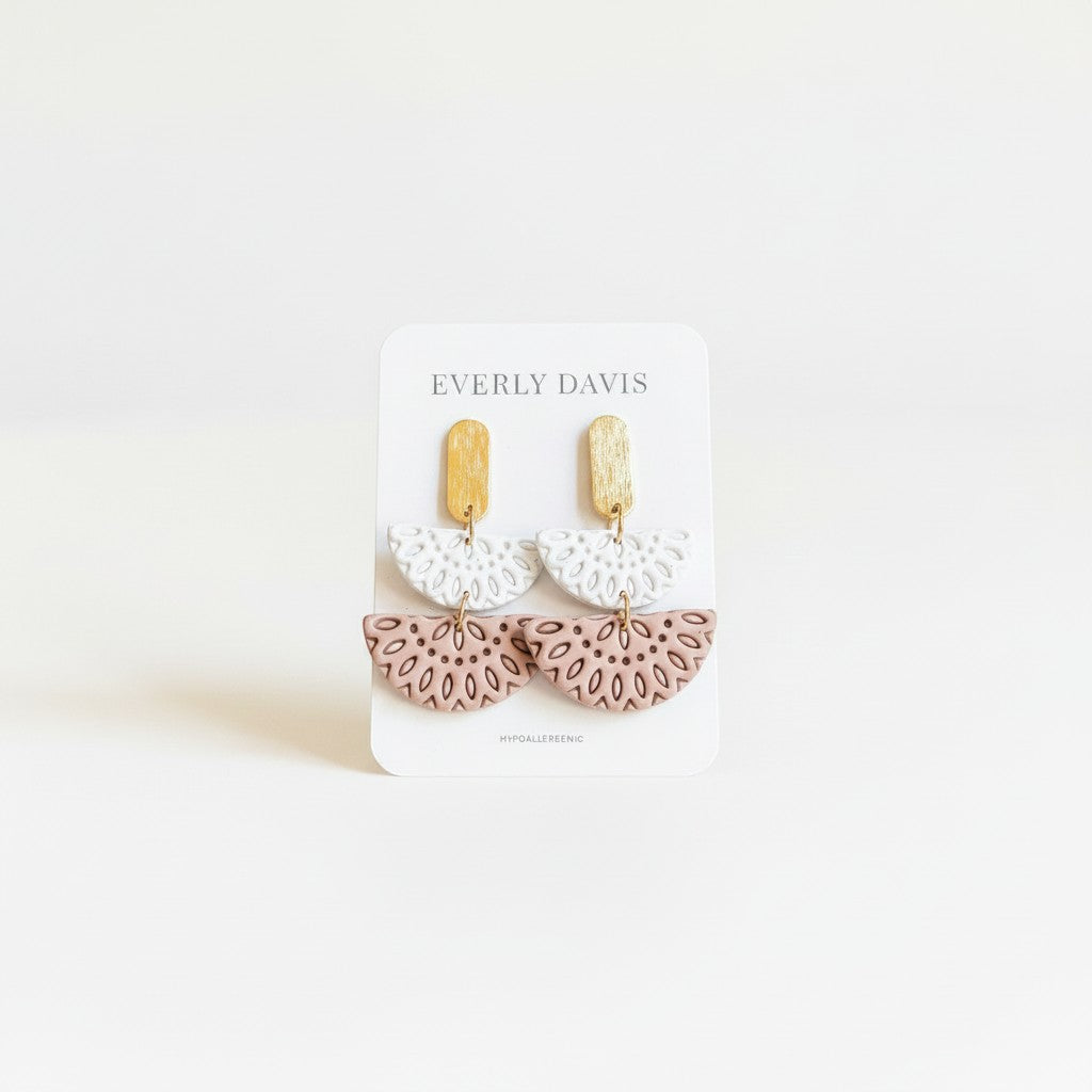 Everly Davis Annie earrings in white and blush pink polymer clay with gold-tone posts. Dangle style with intricate cutout pattern.