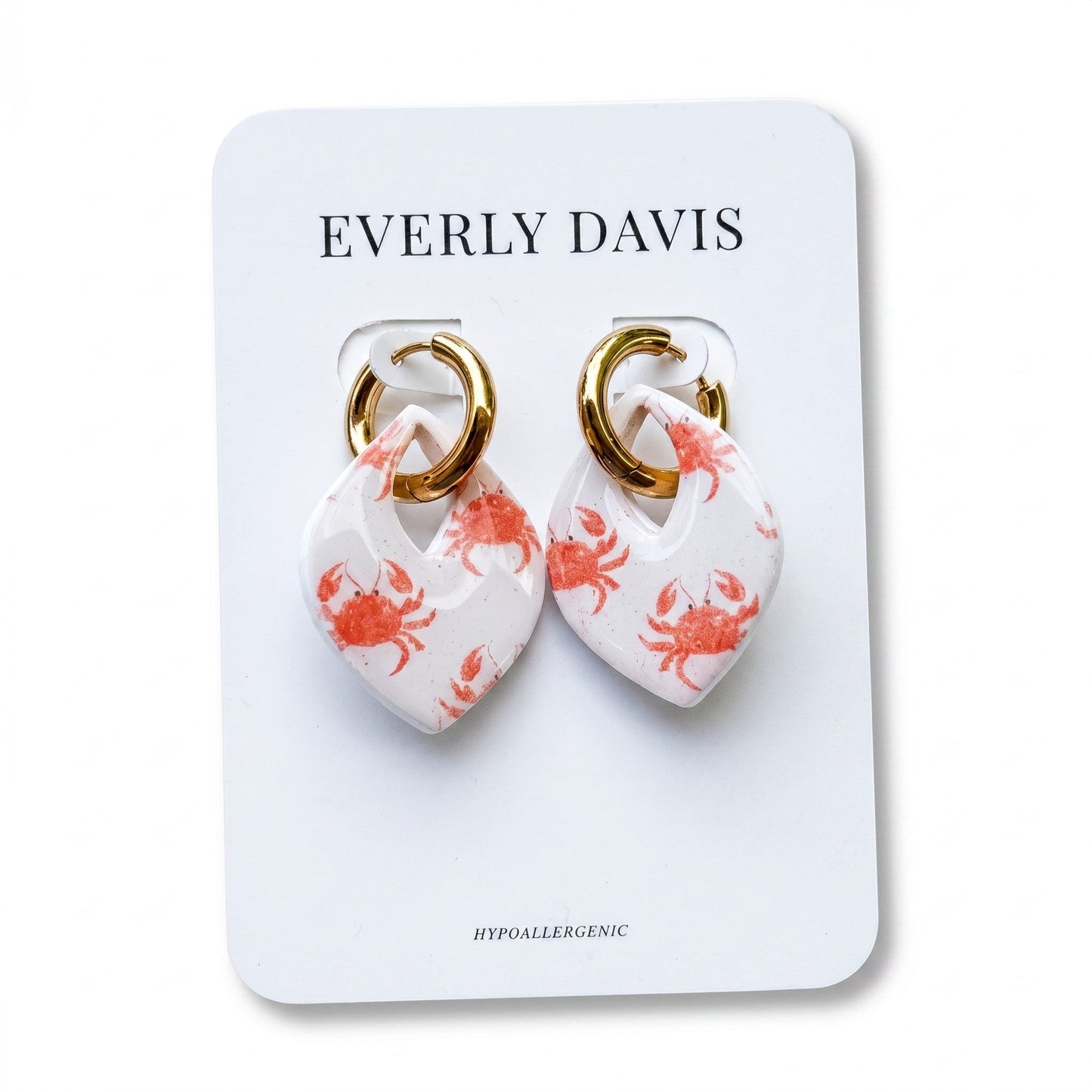 Everly Davis white resin earrings with a glossy finish, featuring a repeating pattern of small orange crabs and gold hoops. Hypoallergenic.