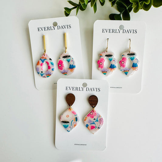 Everly Davis abstract floral dangle earrings in pink, blue, and purple acrylic with gold-tone or wood accents.