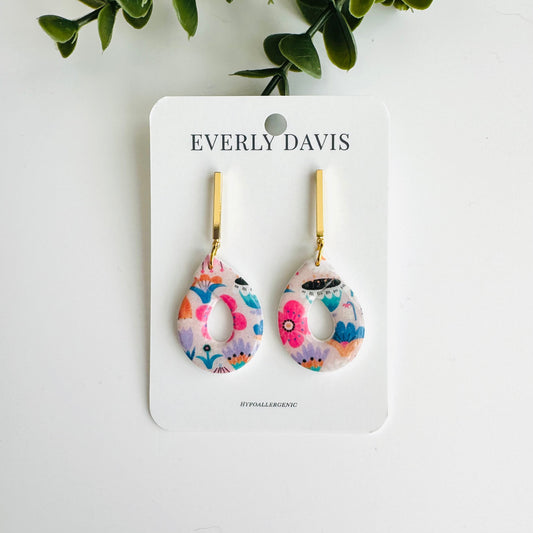 Everly Davis teardrop dangle earrings with abstract pink, blue, and purple floral pattern and gold bar accent.