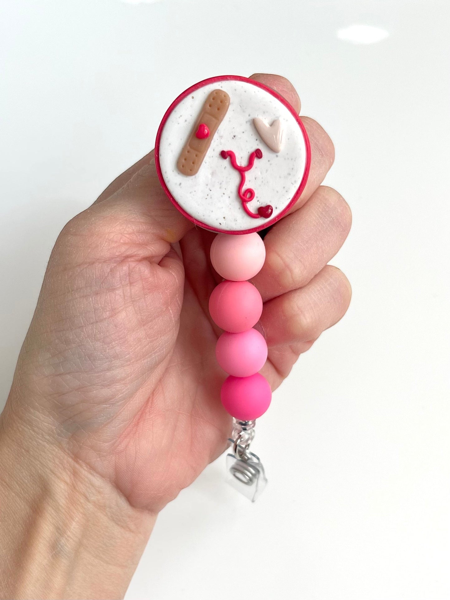 Everly Davis handmade beaded badge reel with medical theme: stethoscope, heart, and band-aid. Pink ombre beads.