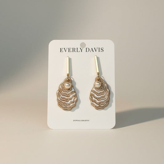 Everly Davis oyster shell dangle earrings with pearl accents. Gold bar hooks and natural shell fragments create coastal elegance.