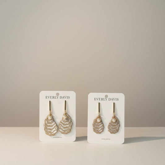 Everly Davis oyster shell dangle earrings with pearl accent. White and gold wavy shell design with gold hooks.