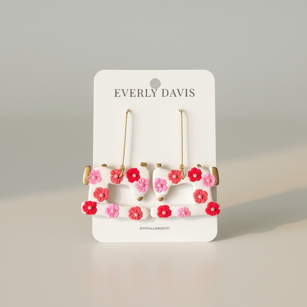 Everly Davis white dangle earrings shaped like sewing machines with pink and red floral accents.