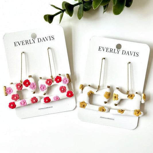 Everly Davis white dangle earrings shaped like sewing machines with pink, red, and yellow floral accents.