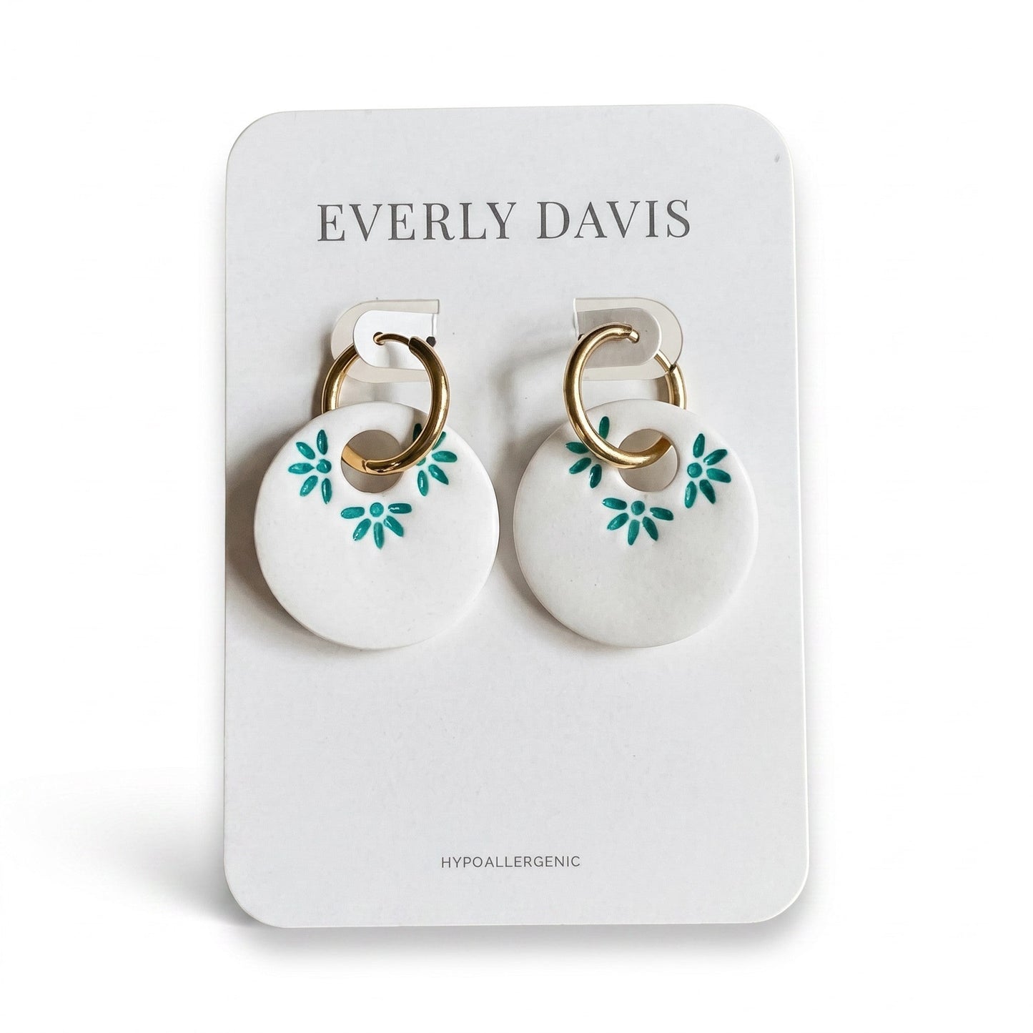 Everly Davis white polymer clay hoop earrings with teal floral imprints and gold hardware.
